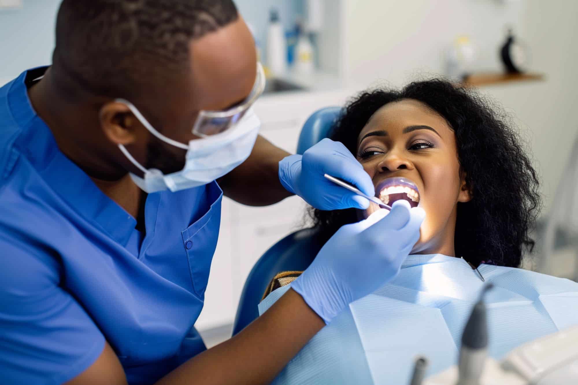 A dentist in blue scrubs is cleaning the teeth of a woman